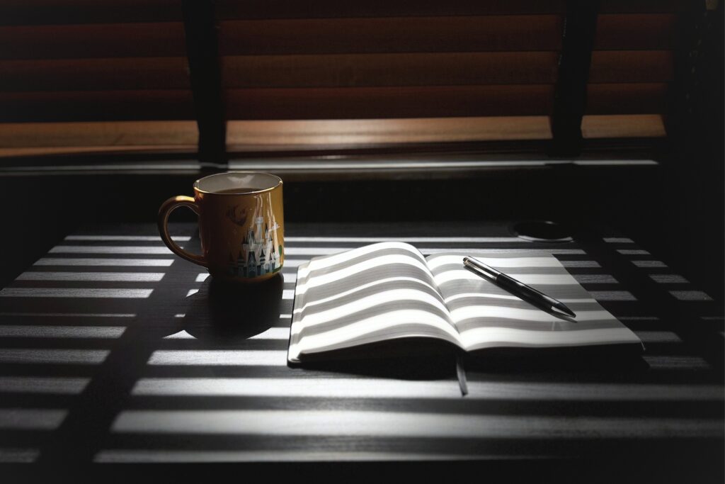 morning light creating shadow over open notebook and pen with a coffee cup sitting on the side