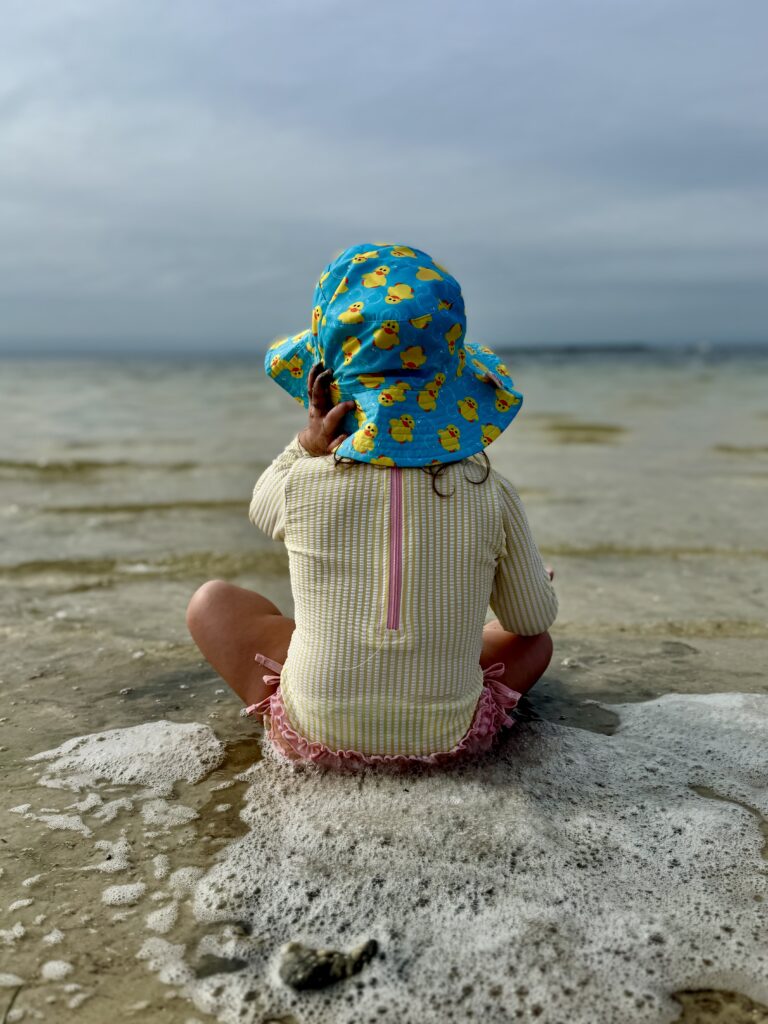 child sitting at shoreline with water and soft natural light