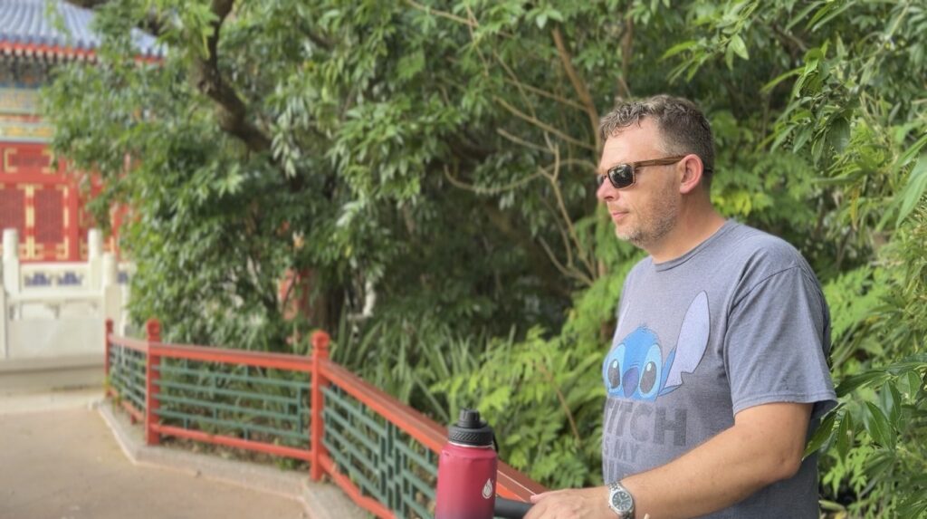 A quiet garden pathway behind the China Pavilion at EPCOT, where a man stands surrounded by lush greenery and reflective stillness, capturing the slower, more restful side of travel.