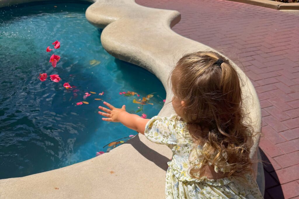 A child in a spring dress throwing flower pedals into a beautiful fountain on a sunny spring day.